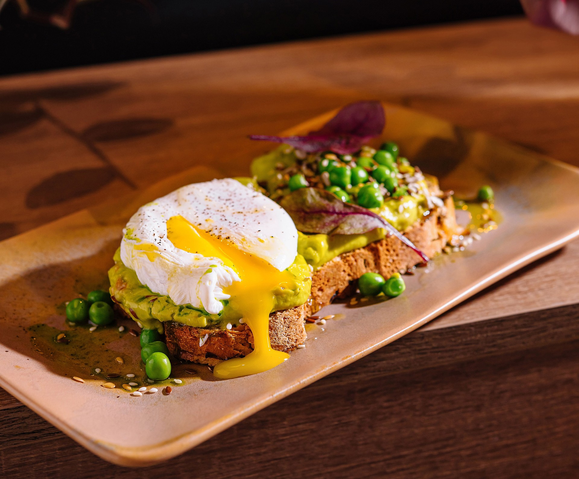 Delicious poached egg toasts with avocado and peas on wooden table