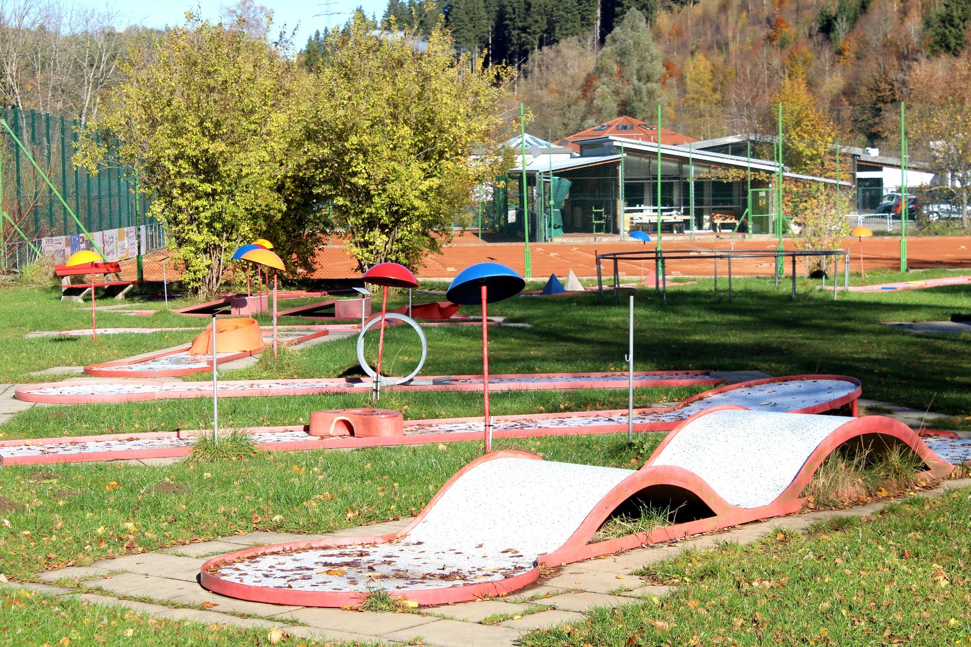 Miniature golf course in autumn, autumn leaves, in the background a tennis court with red sand. Allgäu, Bavaria.