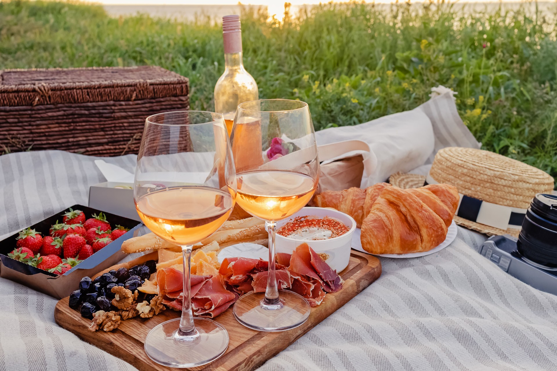 Picnic with strawberries, croissants and appetizers on the board and rose wine.