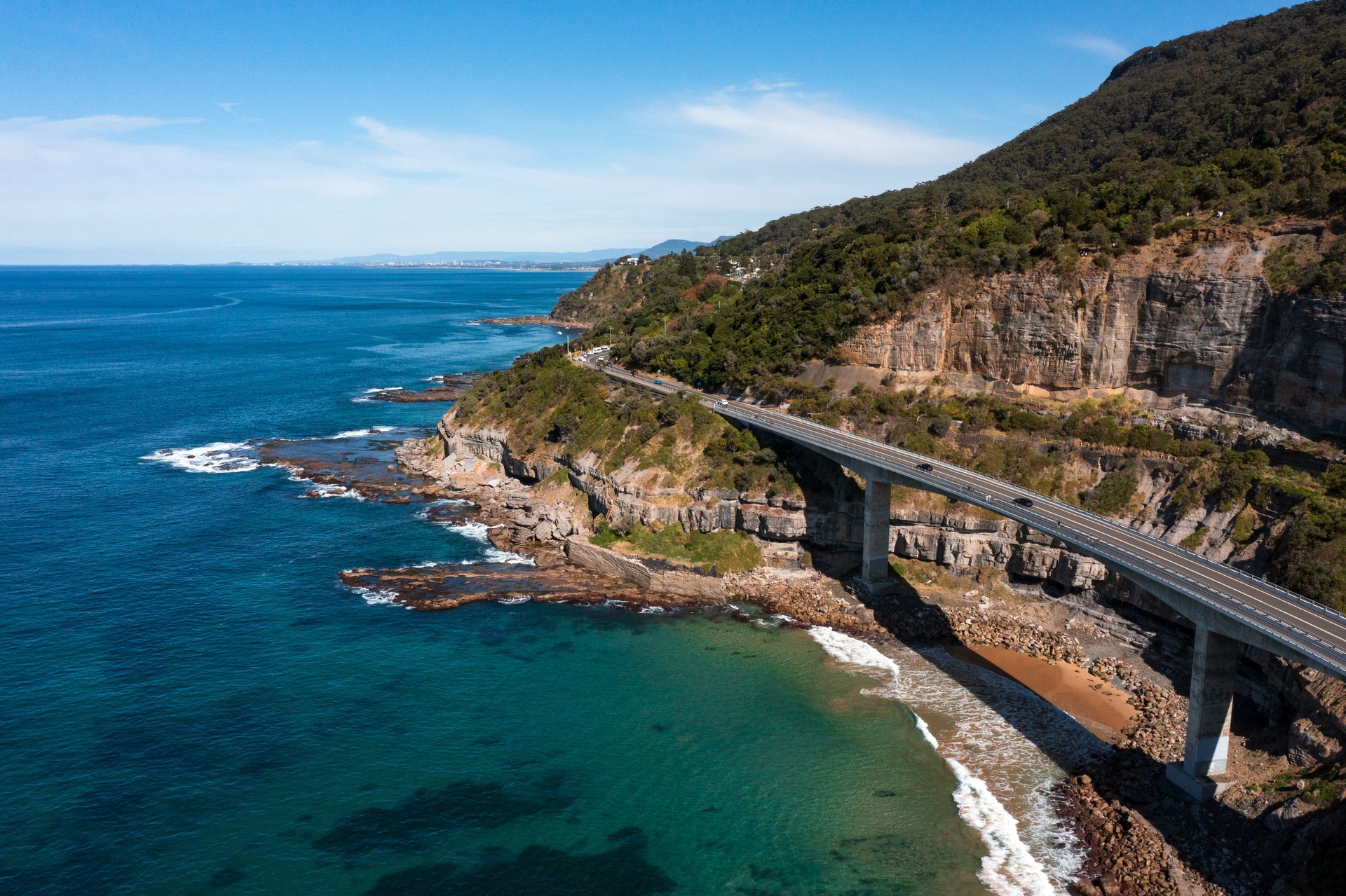 Aerial view of the beautiful Illawarra coastal escarpment featuring the famous Sea Cliff Bridge. Captured from high above a clear blue pacific ocean looking south along the winding bridge to Wollongong.