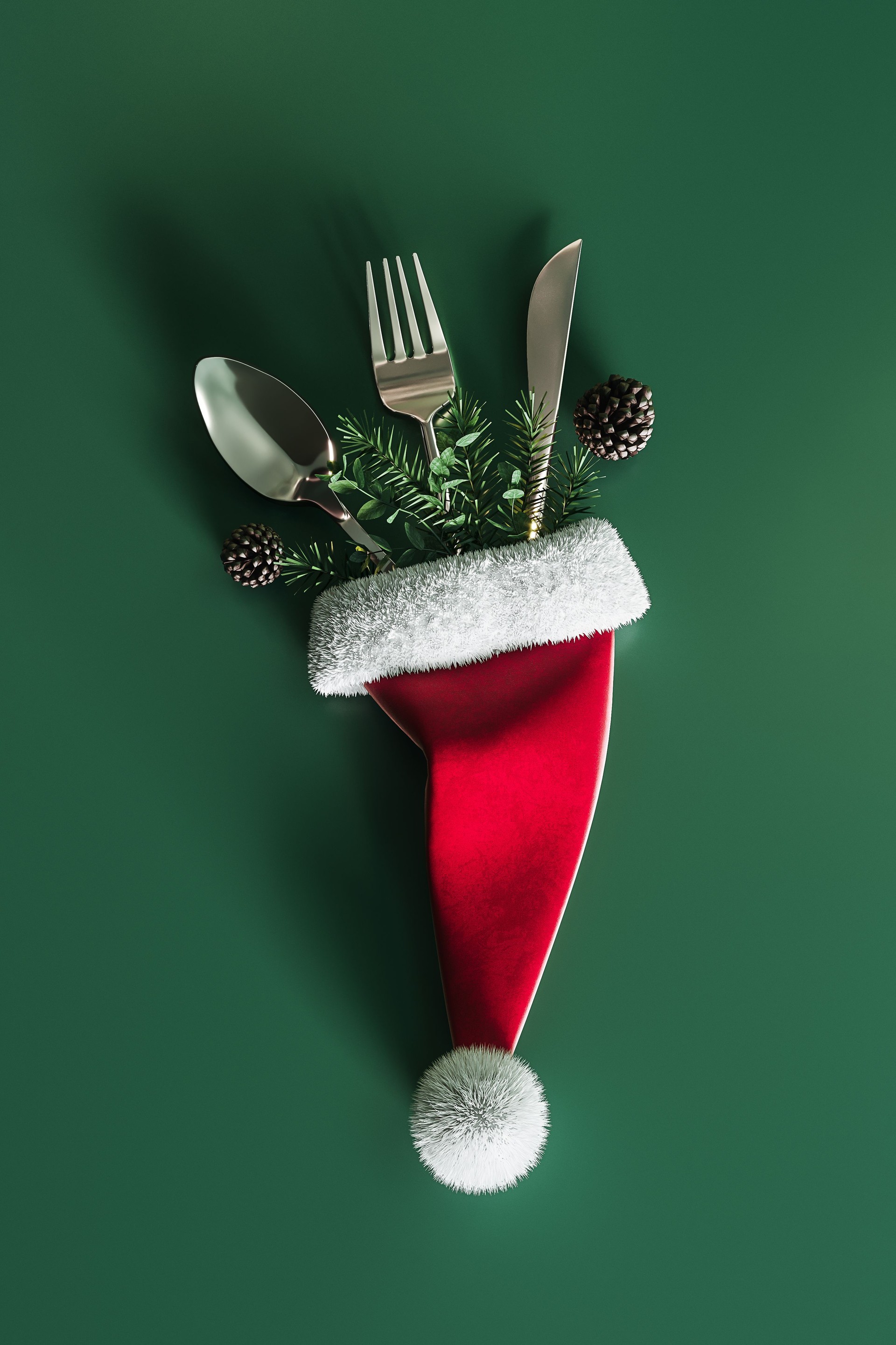 Santa hat with silver cutlery and Christmas decoration on green background. Christmas dinner concept design.