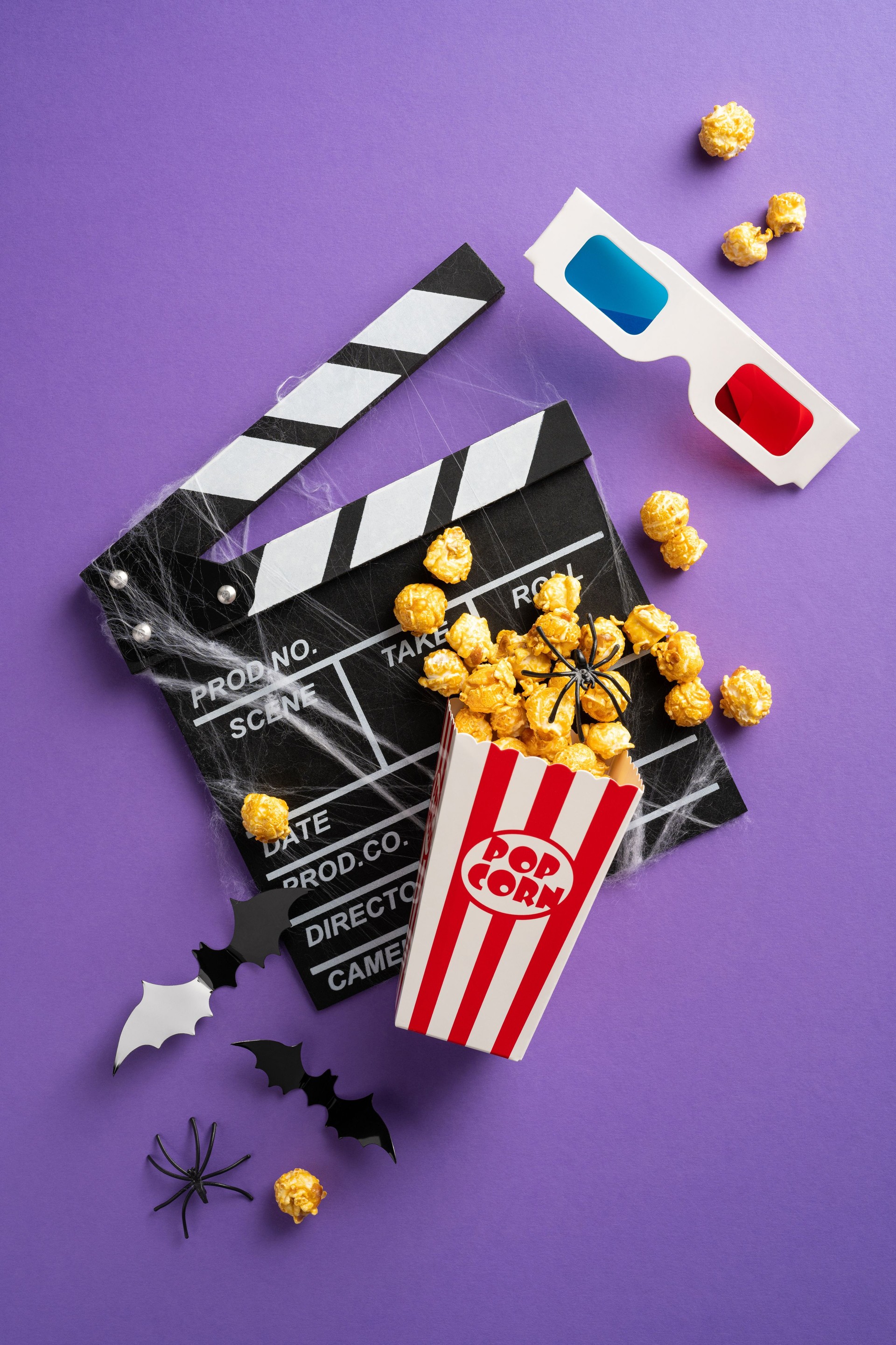 Popcorn, 3D glasses, and movie clapperboard with Halloween decorations on a vertical purple background