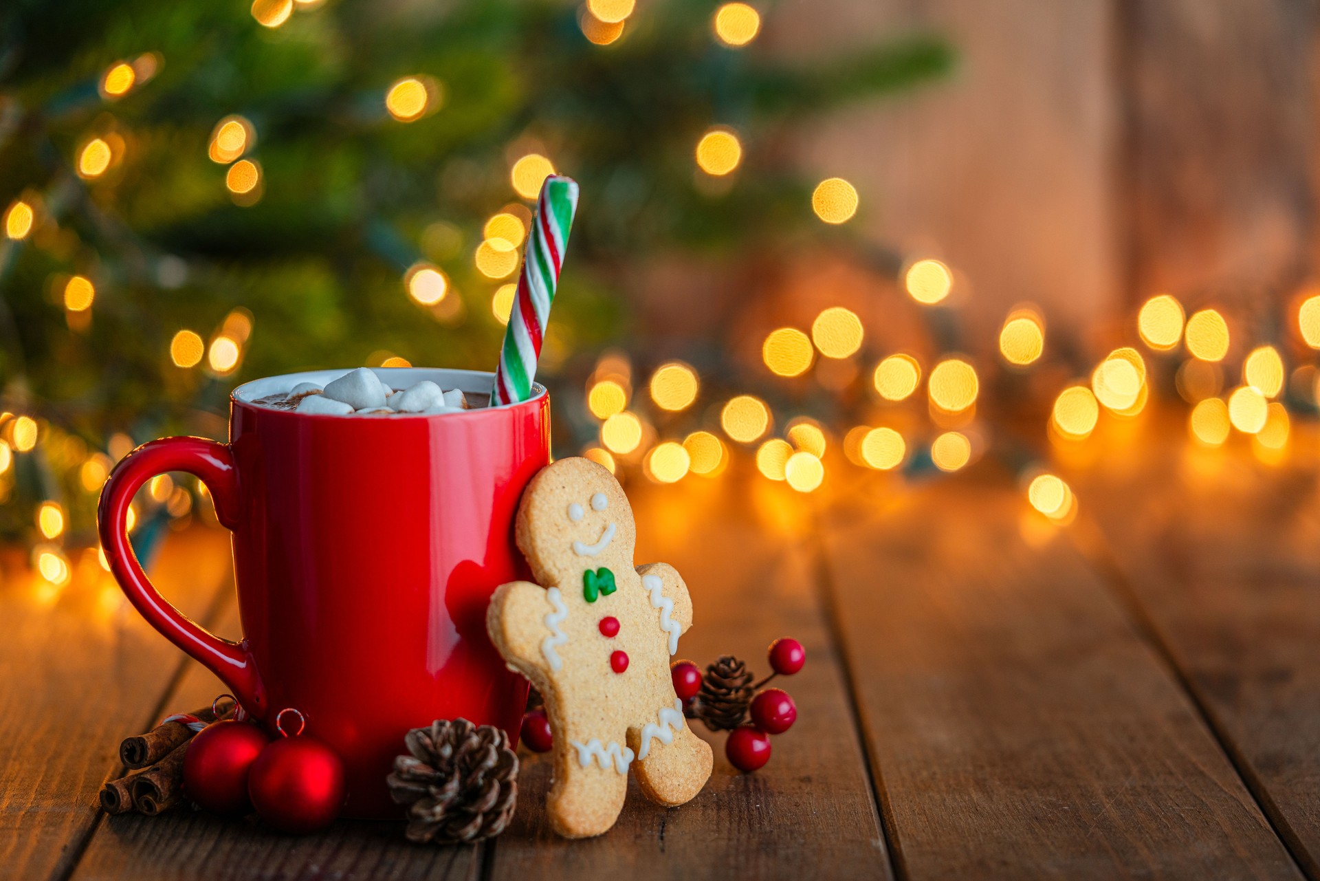 Red mug of hot chocolate with marshmallows and gingerbread man cookie on Christmas table