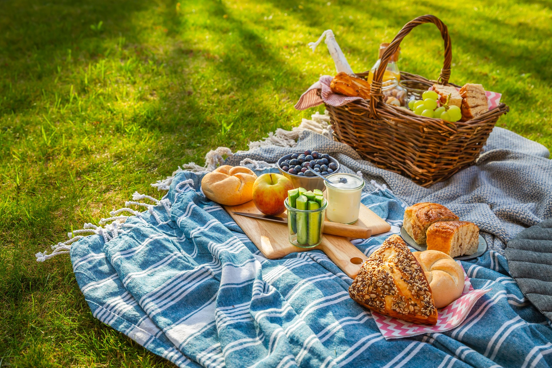 Picnic duvet and basket with different food, fruits, orange juice., yogurt and bread on green grass